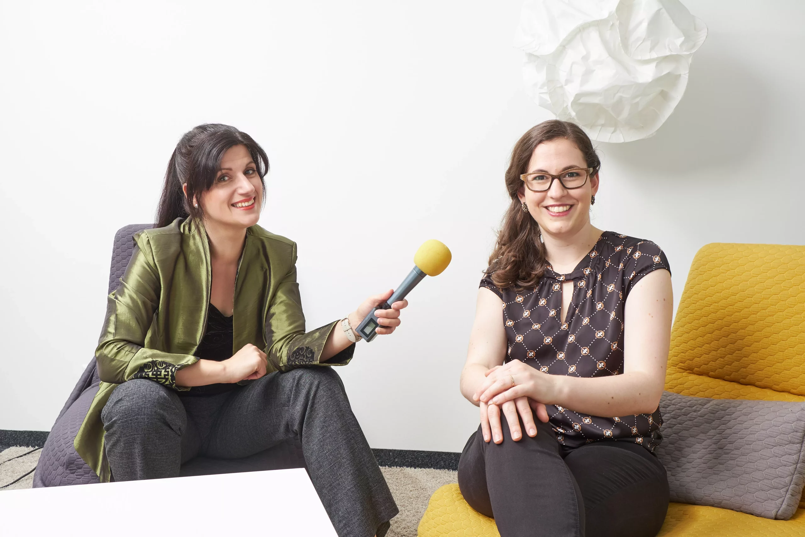 Zwei Frauen auf Hockern mit gelbem Mikrofon